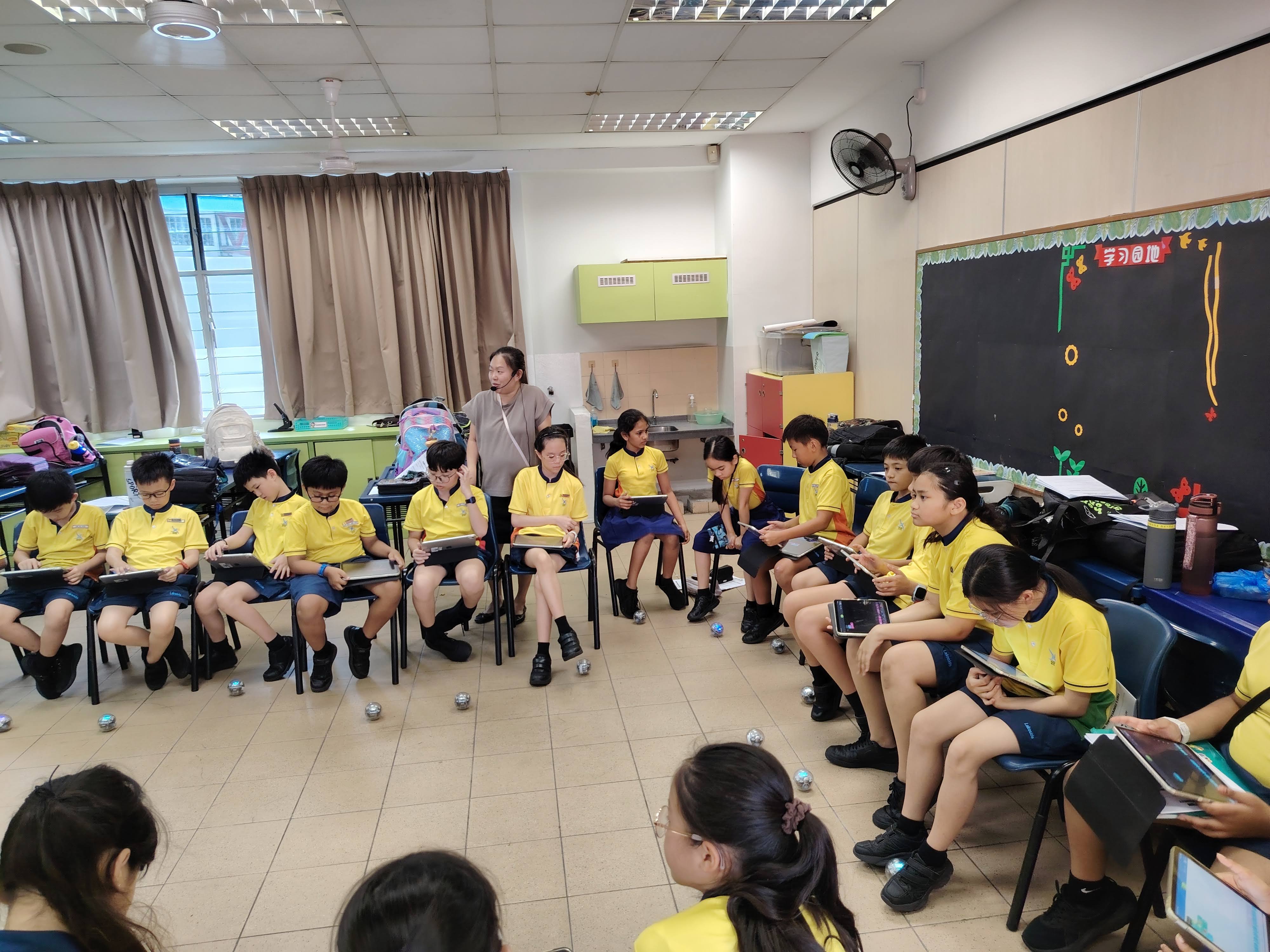 Students sit in a large circle as they program the Spherobots for the first time